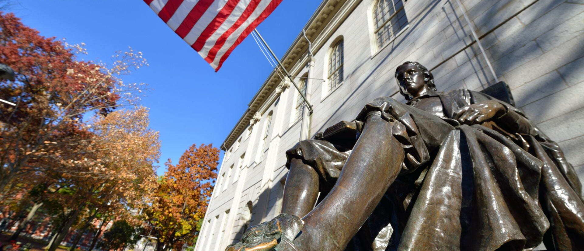 The John Harvard statue on a bright sunny day in Harvard Yard